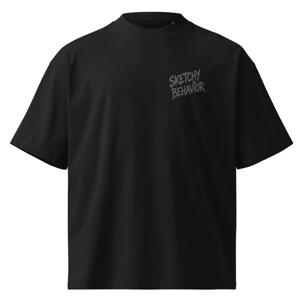 Blaster 2.0 unisex organic oversized high-neck t-shirt in Black, front view — small tonal black-on-black "Sketchy Behavior" spray-style lettering on the left chest